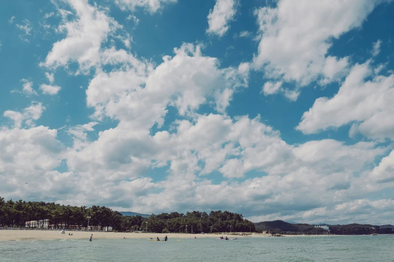 people are out at the beach, while the sky is filled with clouds