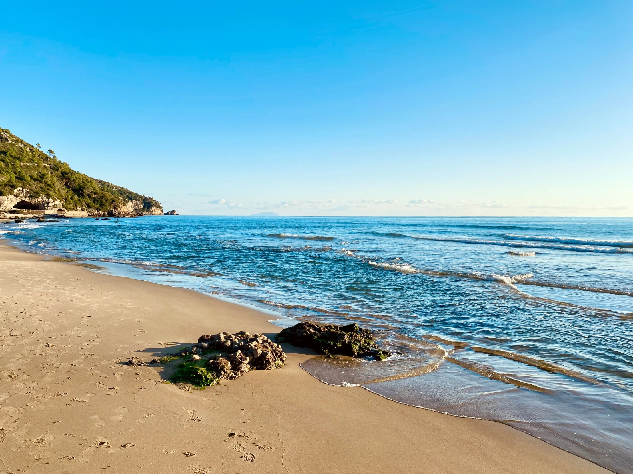 a sandy beach next to the ocean under a blue sky