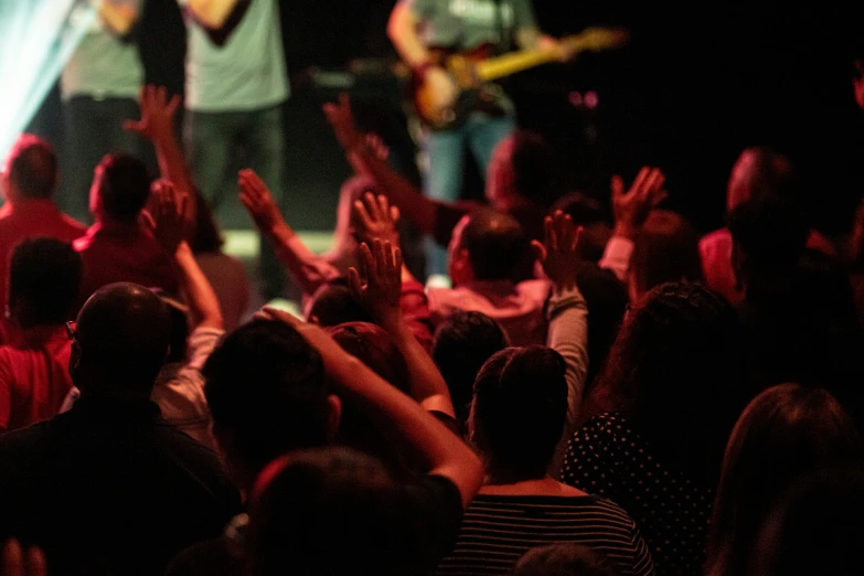 a crowd at a concert with one man on a stage singing and another woman in the front holding up their hands to the microphone