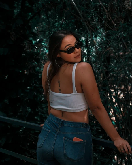a girl in jeans and crop tops standing next to trees