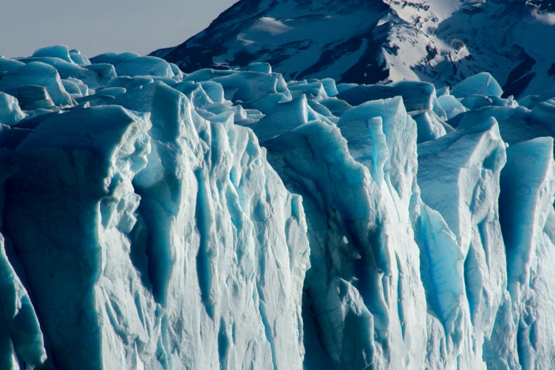 a tall iceberg with snow capped mountains in the background