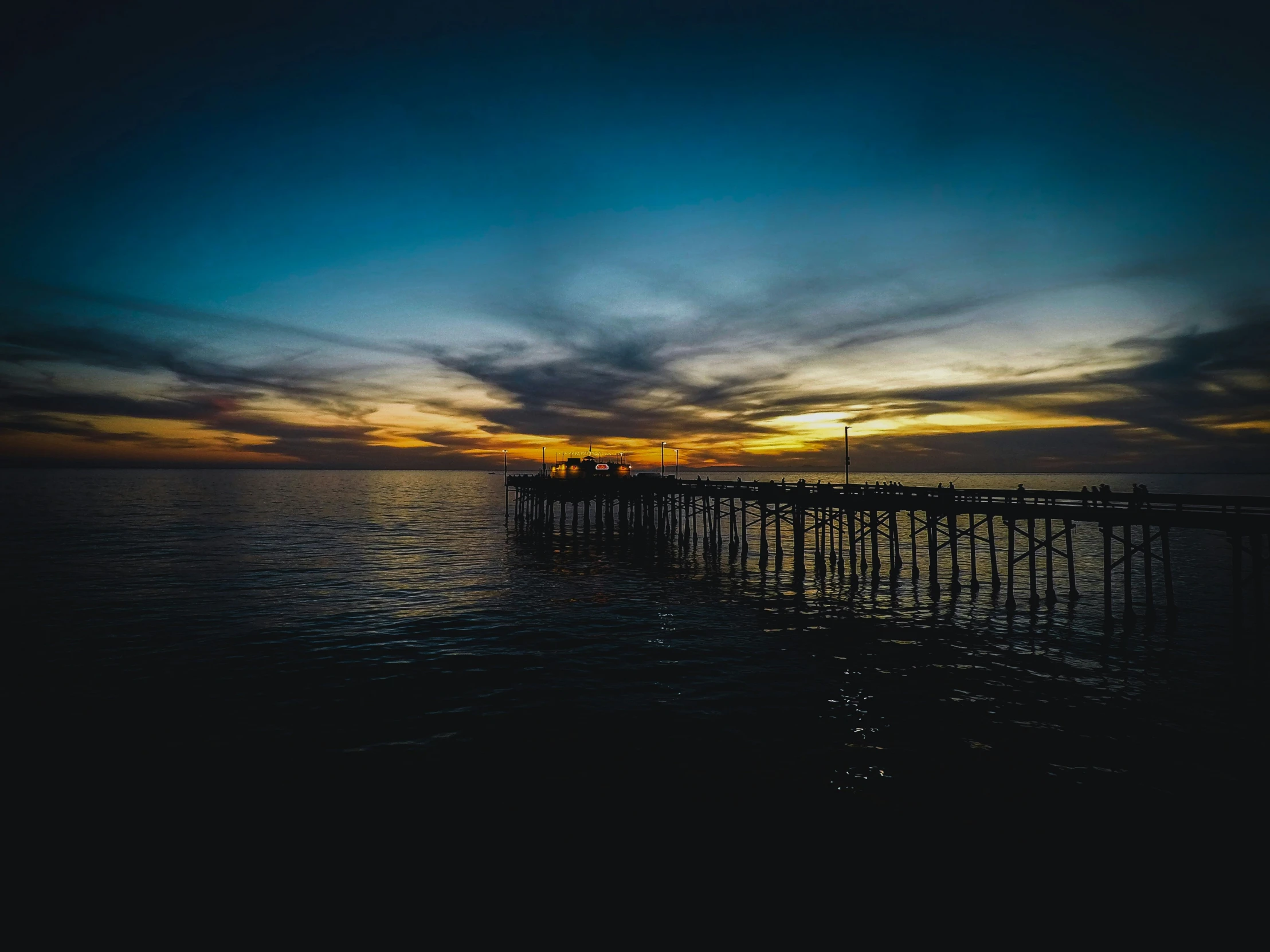 some dark clouds and blue water with a pier at sunset