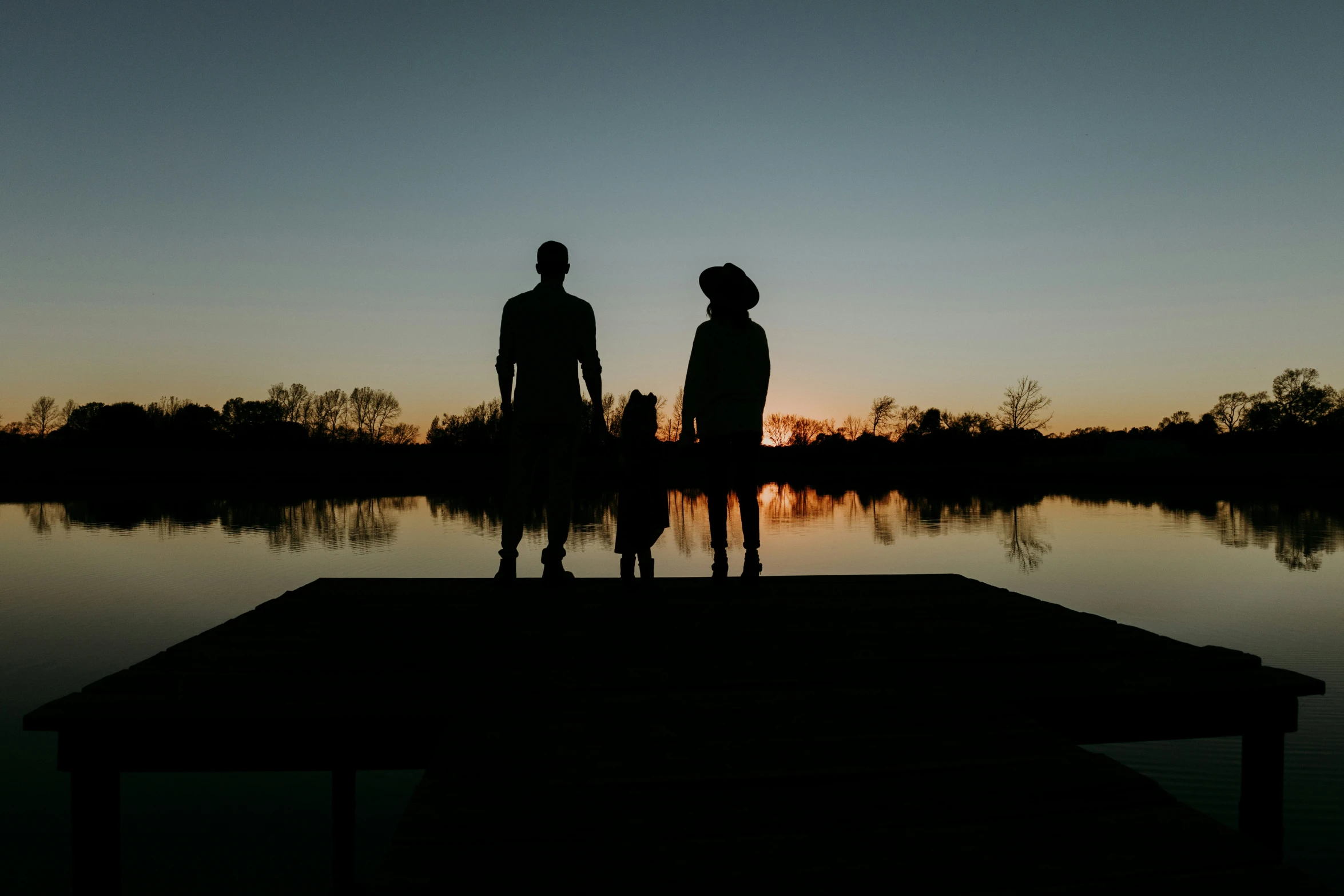 two people standing on the end of a dock next to water