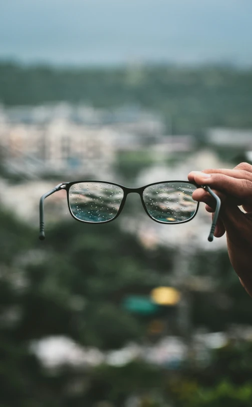 a hand holding glasses while in front of a scenic city