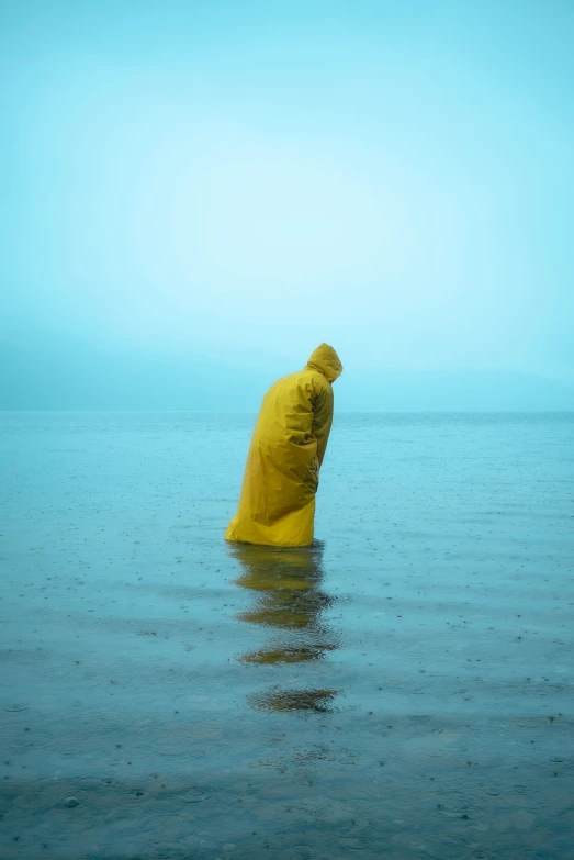a person in yellow stands in water with a blue sky behind him