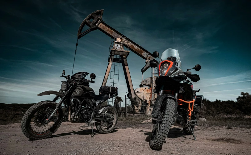 two motorcycle standing near an oil pump in a dirt field