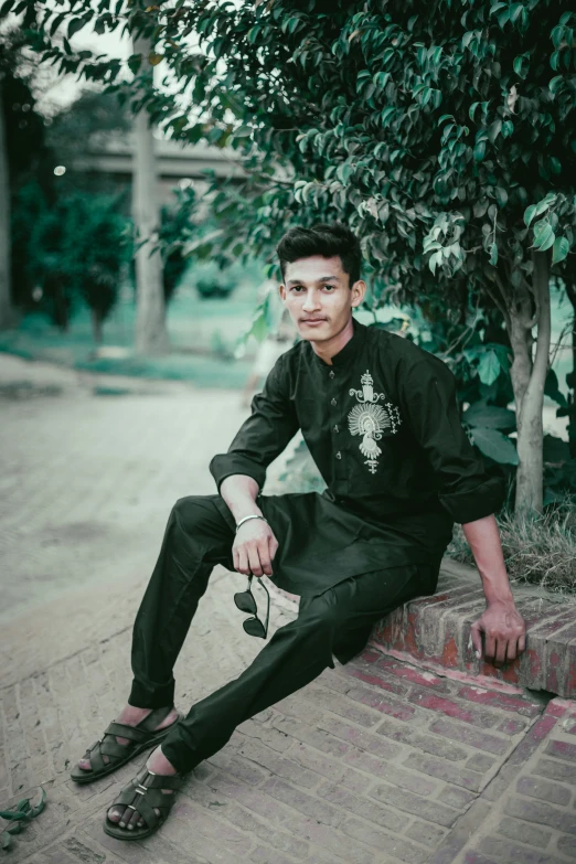 a young man sitting under a tree on the pavement