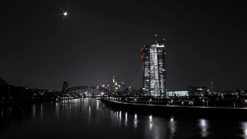 view of large skyscr at night from a river near a bridge