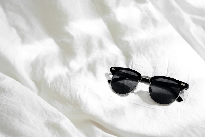 some sunglasses on a white sheet on a bed