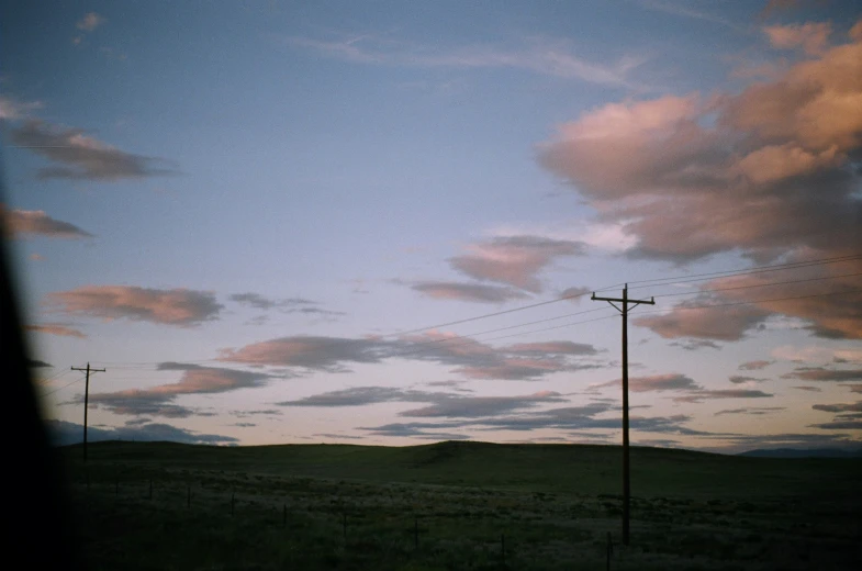 a sunset with several telephone poles and grassy field