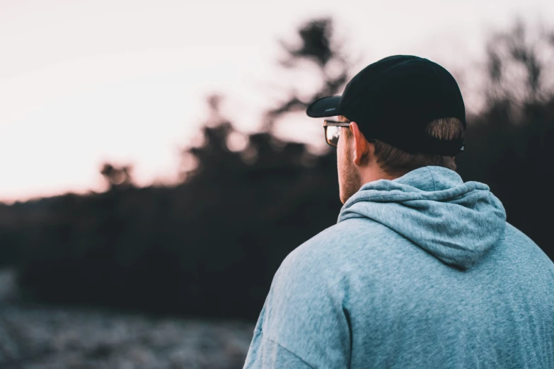 a person wearing glasses and a hoodie looking out into the distance