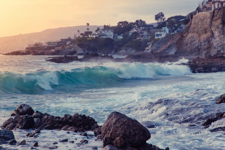 waves crashing on rocks near a cliff in front of houses