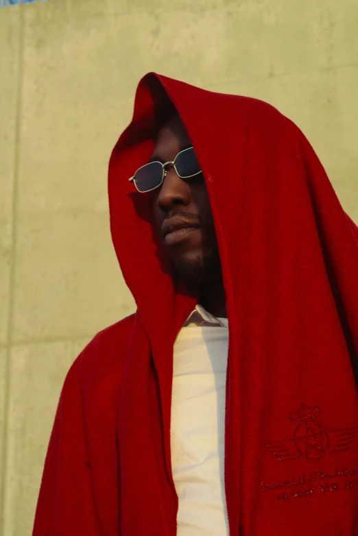 a man in sunglasses stands under a red blanket