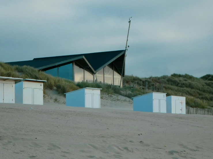 the grass covered hill has blue sheds set on the sand