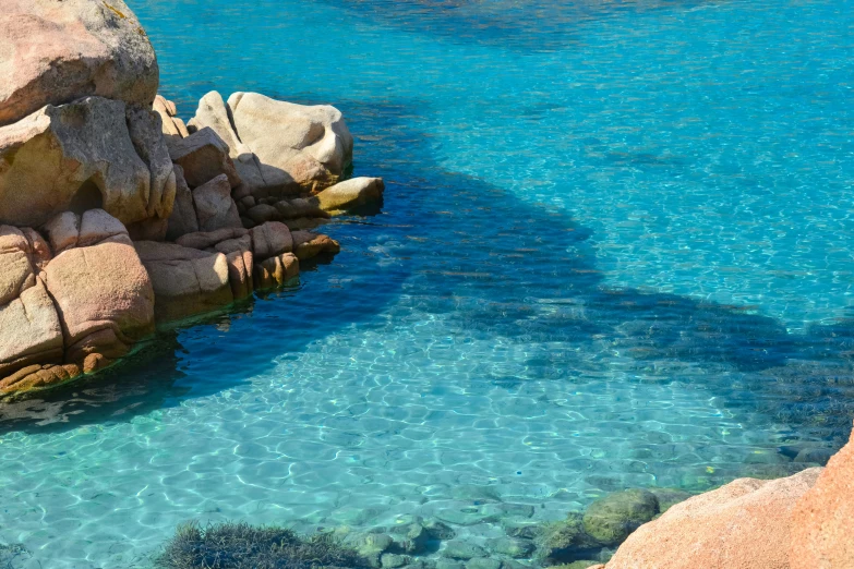 the water is crystal blue next to large rocks