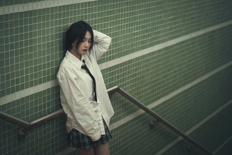 a young woman in an unoned shirt and tie leans on a wall