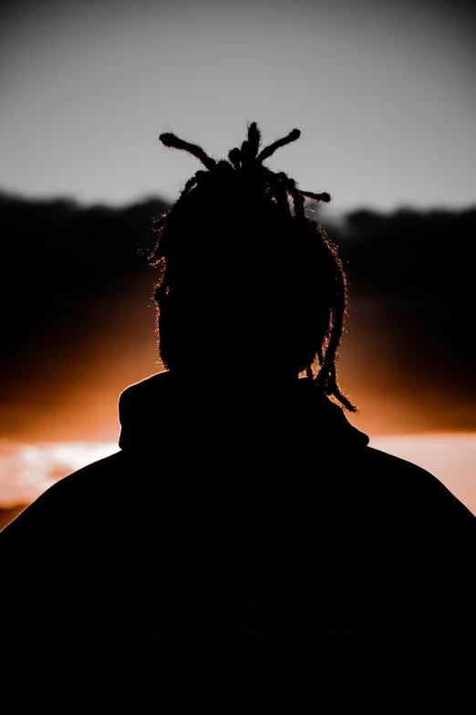 a man with a hat and long hair is shown silhouetted against the sunset