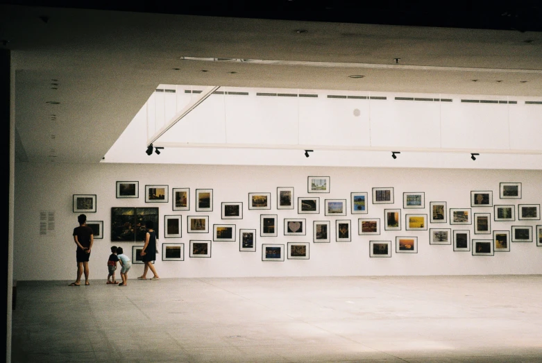 three people standing next to a white wall covered in pictures