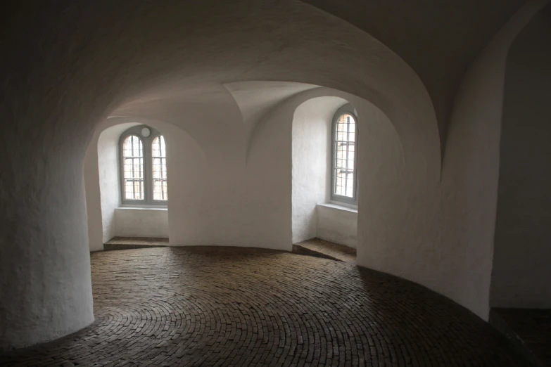 a stone floored room with three arched windows