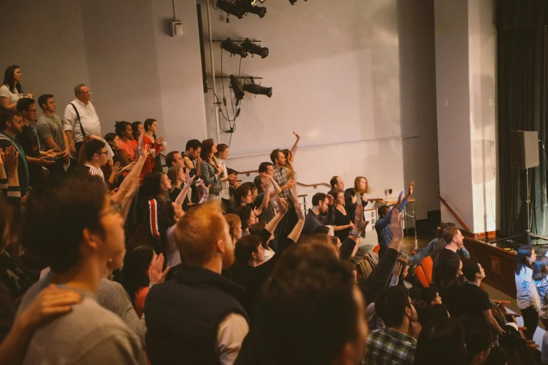 a crowd of people are sitting in a room as one man is raising his hands up