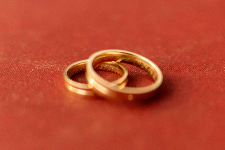 two gold rings with one larger ring on red surface