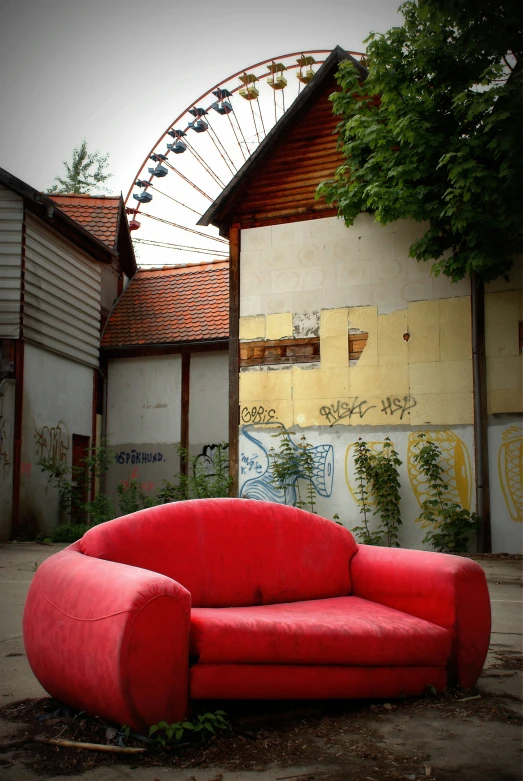 a red sofa sitting outside a building with a ferris wheel in the background