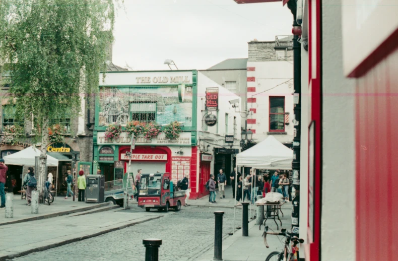 a crowd of people walking down a street with shops and cars