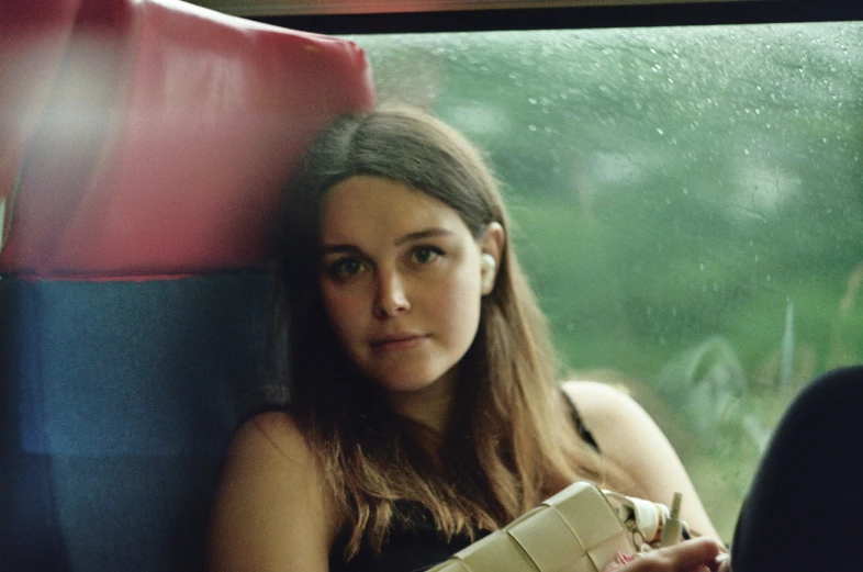 a pretty young lady sitting next to a window with a bag