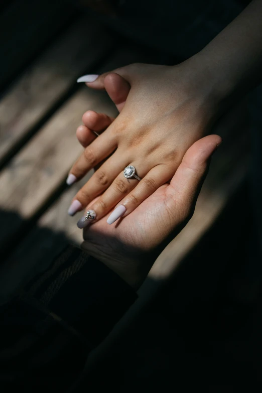 woman's hands holding onto a wooden bench wearing an engagement ring