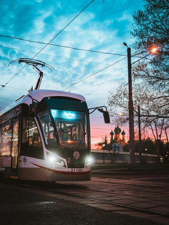 a light rail car with lights on under power lines