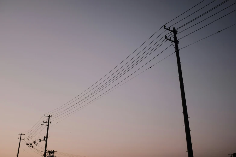 many electric wires hang on the telephone poles against a sunset sky