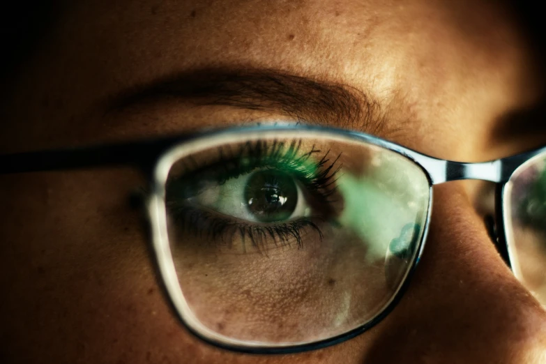 close up of an eye with glasses on and green reflection