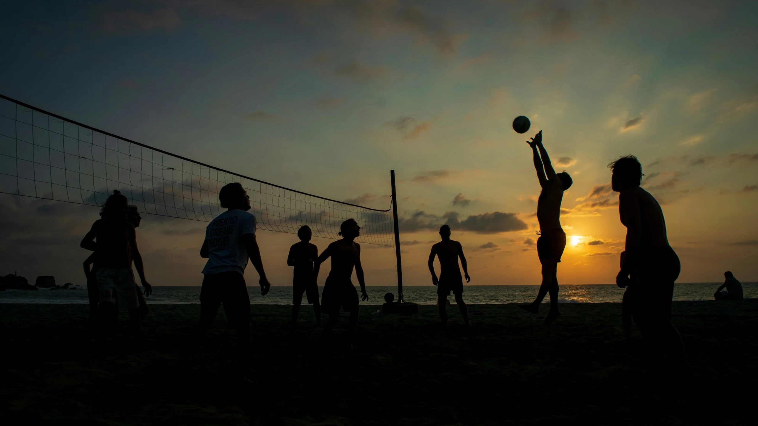 volleyball players are silhouetted against the sun as they play on the beach