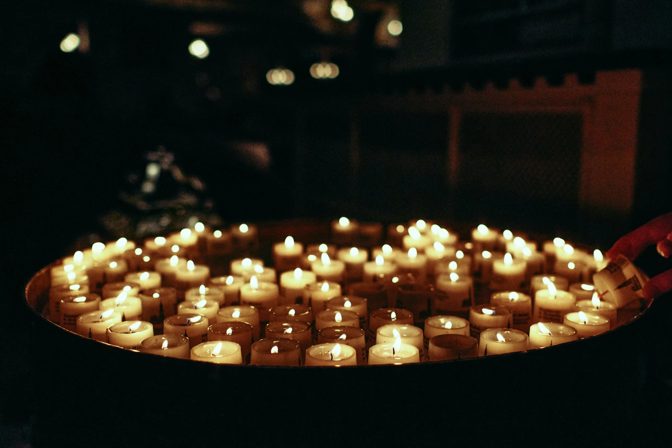 people hold their hands next to a tray with rows of lit candles