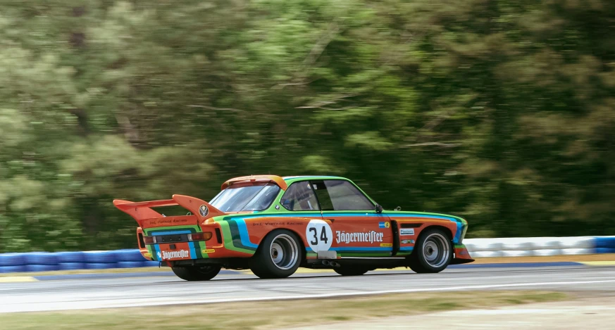 a multi - colored car driving down a road next to forest