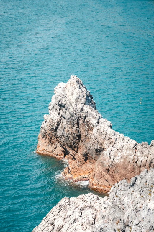 a rock outcropping in the water with a yellow bird flying above it