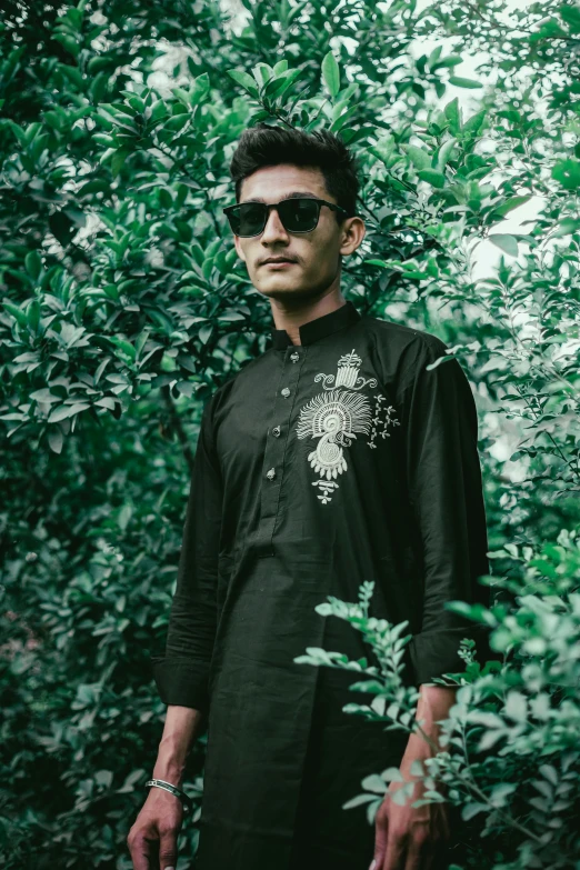 a man with sunglasses and black outfit in front of green plants