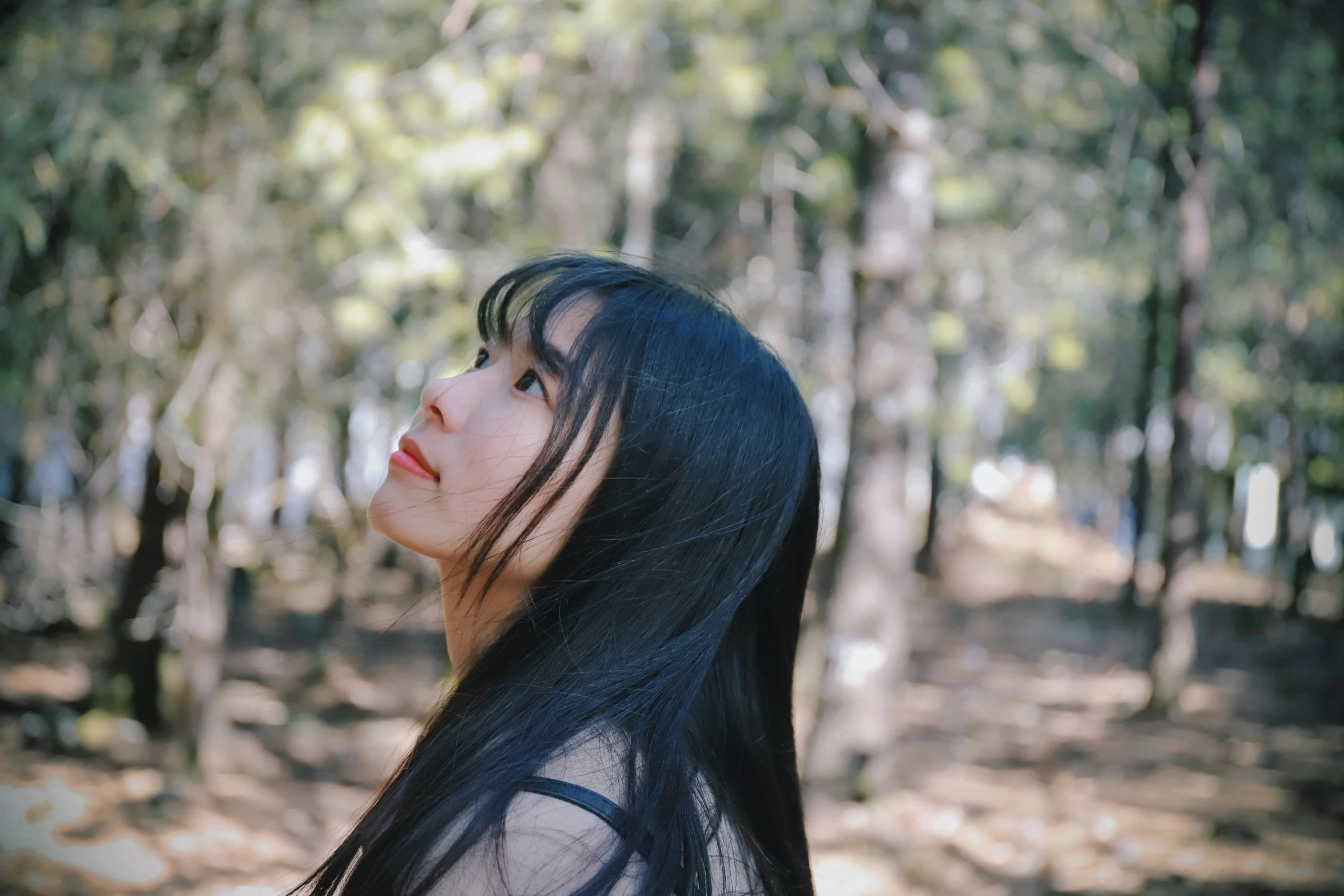 a woman stands in the woods looking up at soing