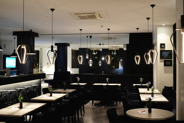 a restaurant with black tables and chairs with lights on their ceiling