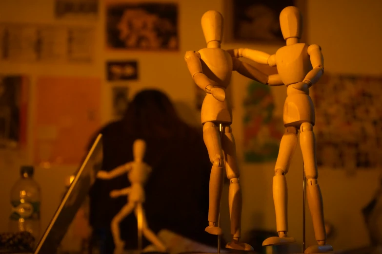 a wooden mannequin couple leaning back against a desk