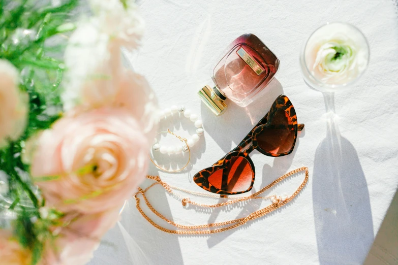 two sunglasses and a glass with perfume on a table