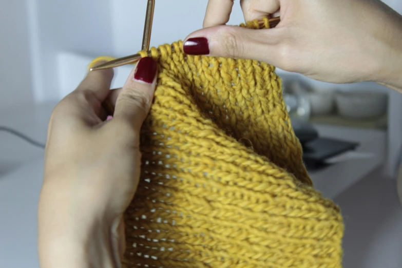 a pair of hands crocheting a yellow sweater with a red handle