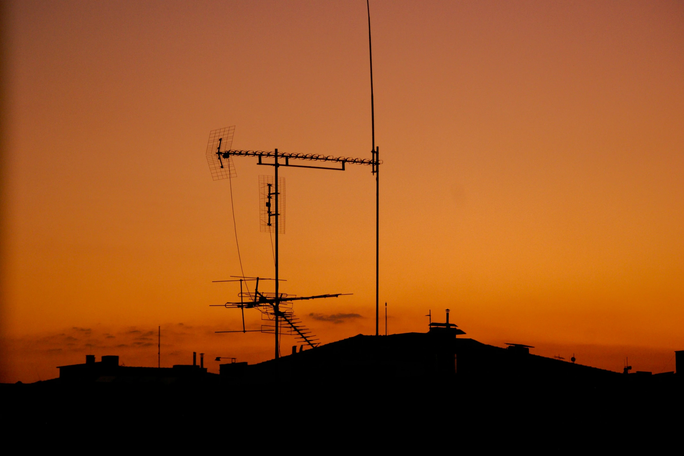 the sun sets behind a building with a tall antenna