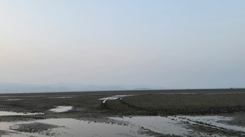 two people are walking in the mud near some water