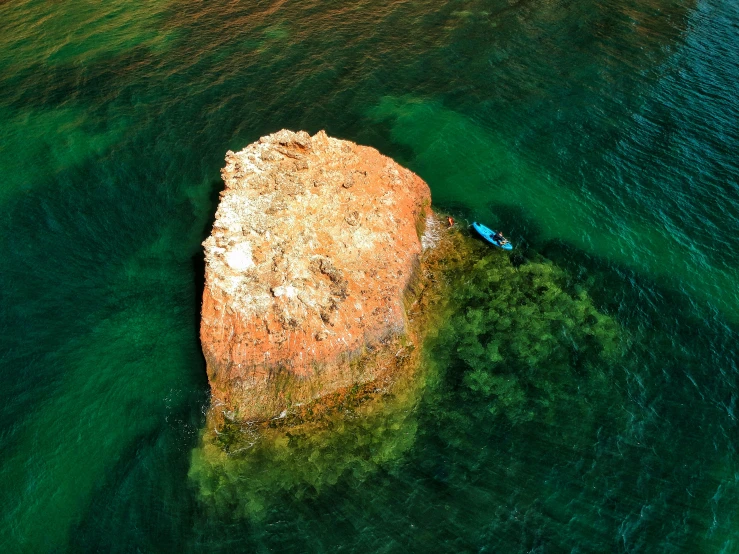 an aerial view of a boat near a large rock in the water