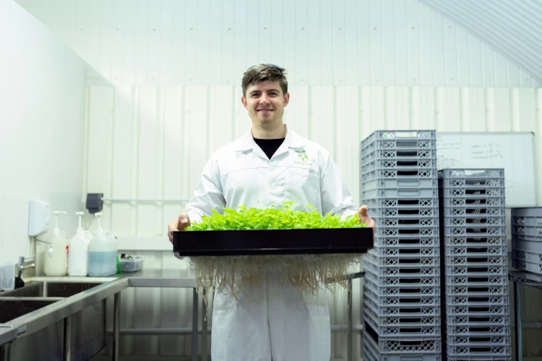 a male in a white coat a shelf and some greens