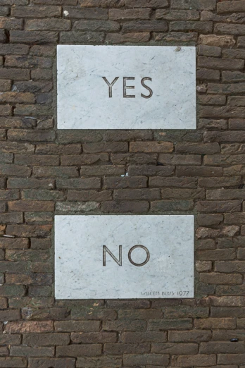 two signs reading yes and no are on the brick wall
