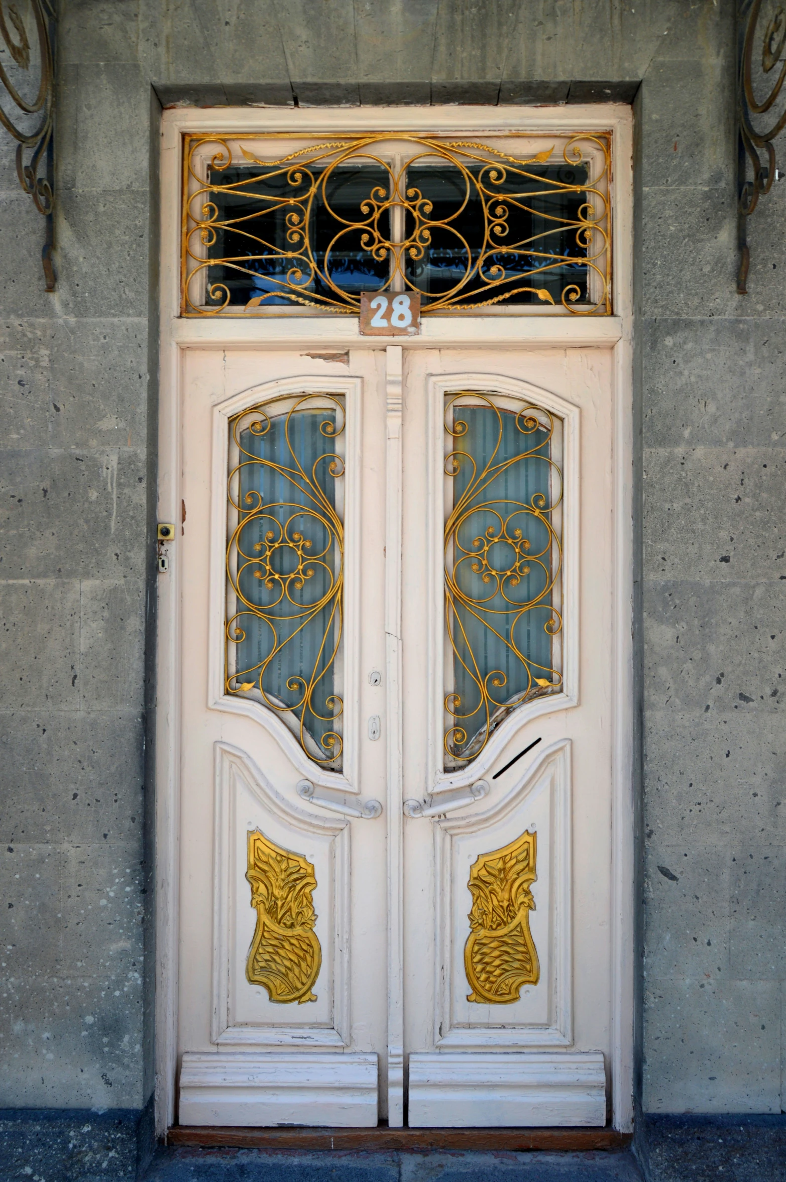 an ornately decorated double white door in front of a stone wall