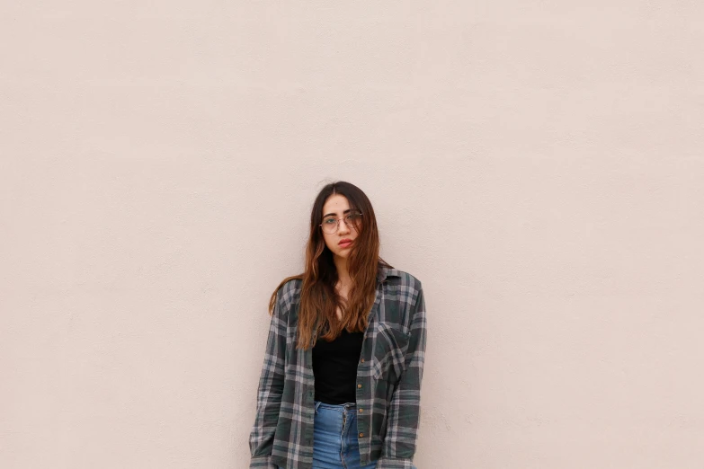 a woman standing by a white wall in a jacket