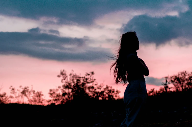 the woman is silhouetted against an intense sky
